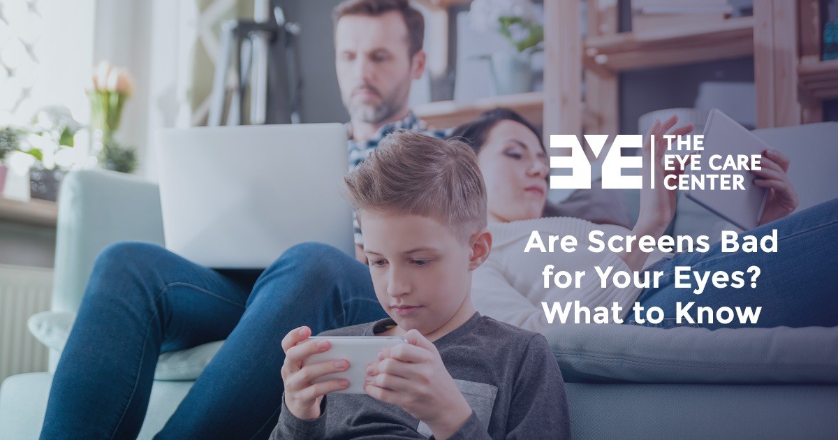 A boy uses a smartphone while adults behind him use a laptop and tablet at home.