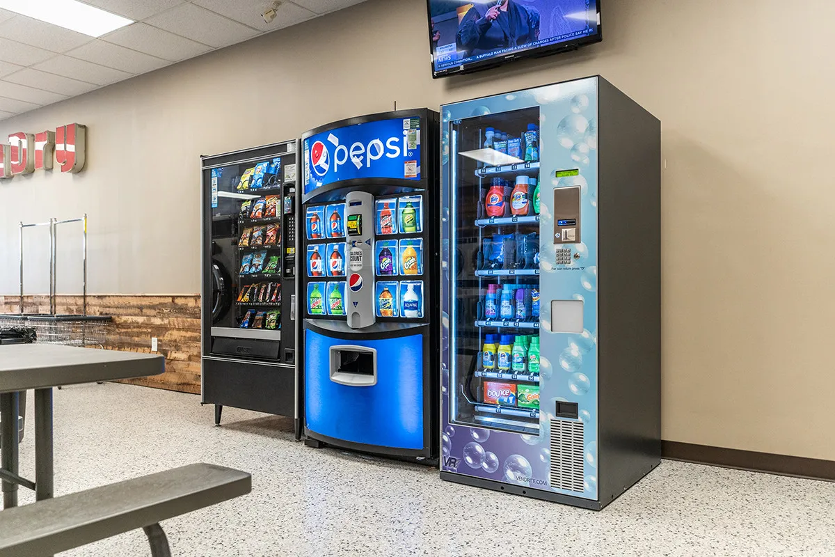 Three vending machines with snacks, drinks, and laundry products.