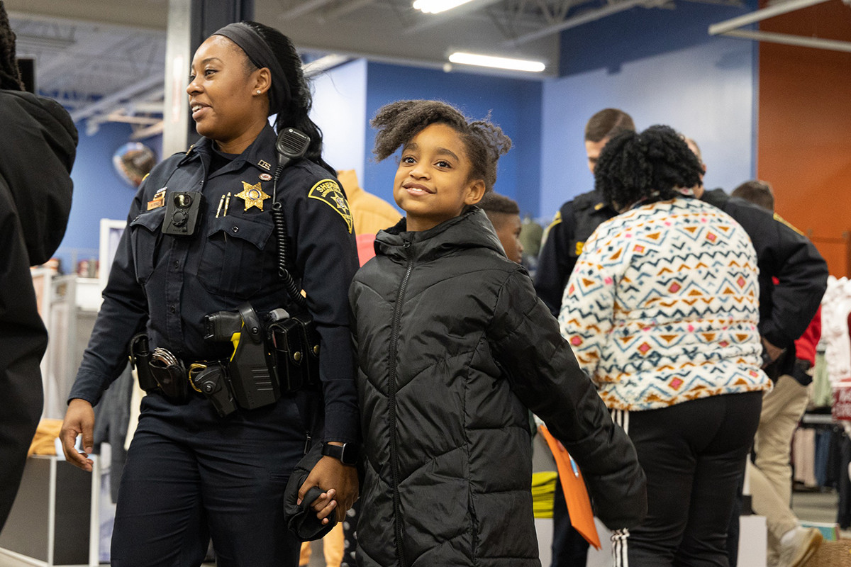 police officer smiling and holding hands with a young girl in a coat at a community event