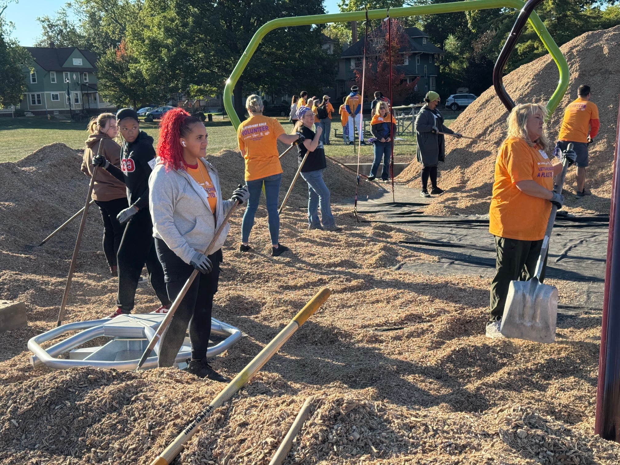 Volunteers with shovels spread mulch under a playground under construction