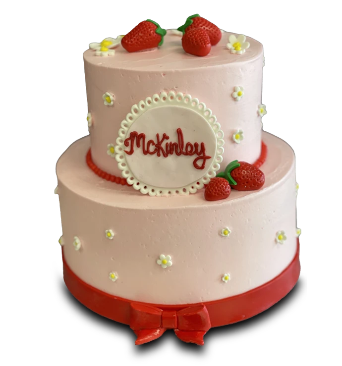 Two-tier pink cake with strawberries, daisies, red bow, and McKinley written on a plaque.