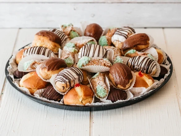 A platter of assorted Italian pastries with chocolate, cream, and powdered sugar on a white table.