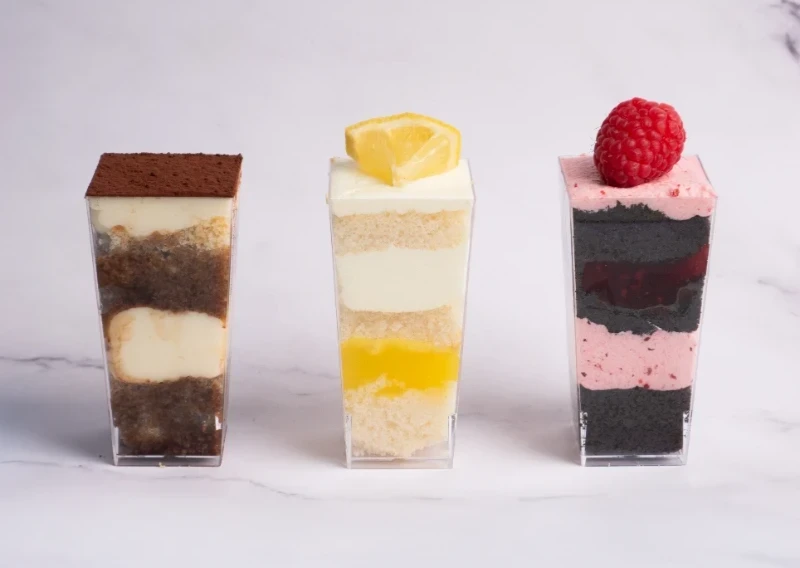 Three layered dessert parfaits in clear cups, each topped with fruit or cocoa powder.