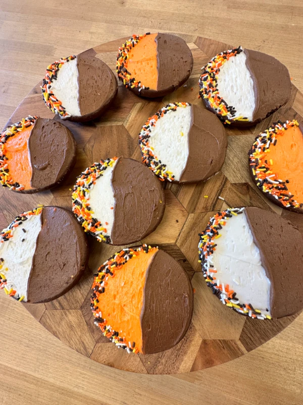Round cookies with half chocolate, half orange or white frosting, and sprinkles on the edges.
