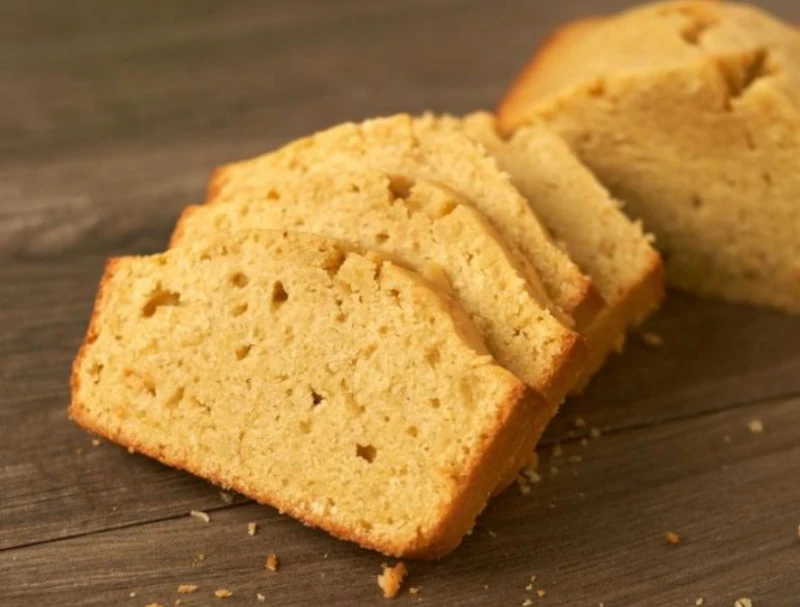 Three slices of pound cake on a wooden surface, with the rest of the loaf in the background.