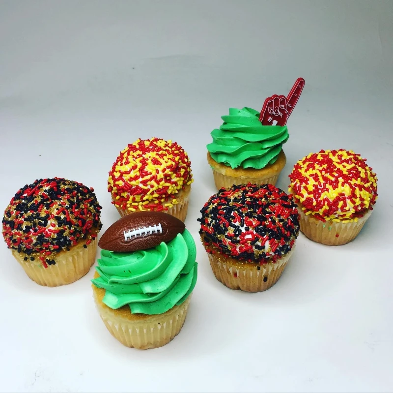 Six cupcakes with red, yellow, and black sprinkles, green icing, and football-themed toppers.