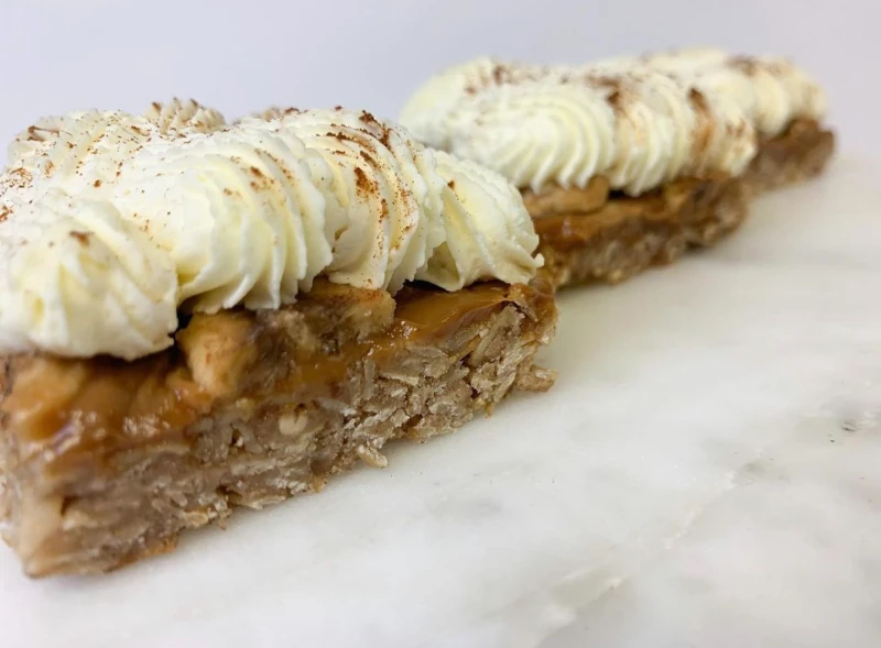 Two oat and caramel dessert bars topped with piped whipped cream and a sprinkle of cinnamon.