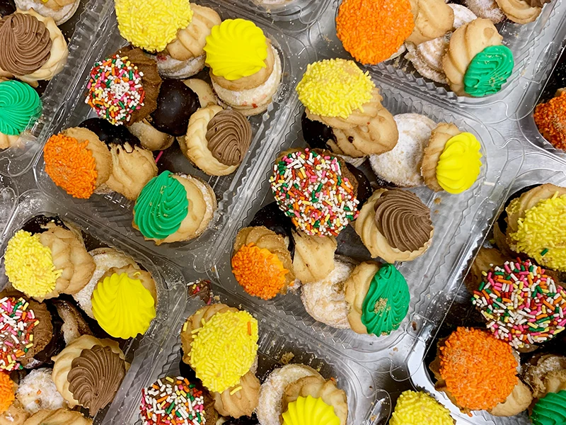 Assorted colorful cookies with sprinkles and frosting in clear plastic containers, viewed from above.