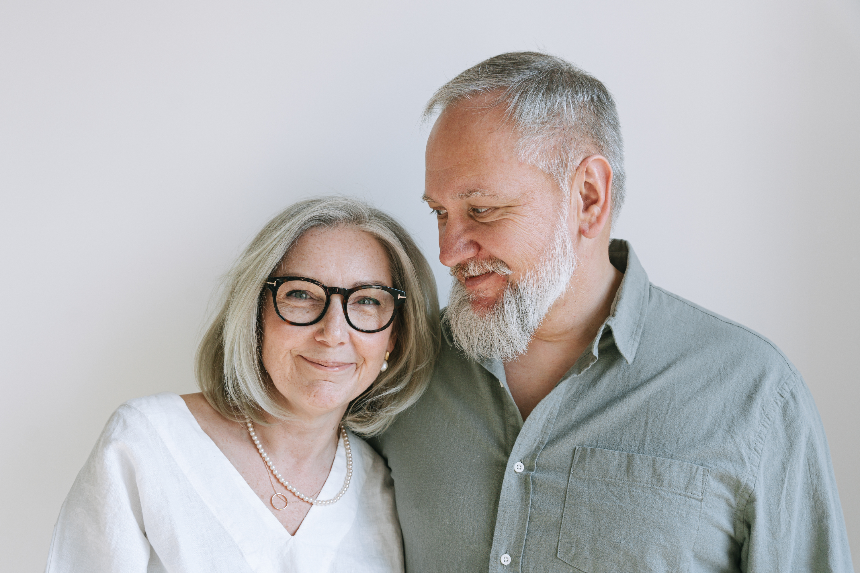 Smiling older couple standing close together against a plain light background.