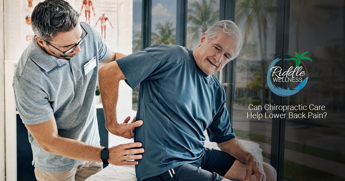 A chiropractor examines an older mans lower back as he sits on an exam table, smiling.