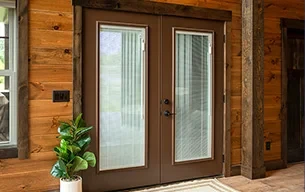 Brown residential entry doors with glass panes, beside a potted plant in a wood-paneled room.