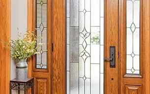 Residential entry doors in Rochester NY with decorative glass panels and a vase of flowers nearby.