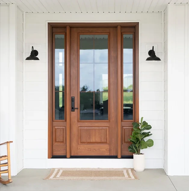 Brown wood front door with glass panels, a potted plant, and two black wall sconces.