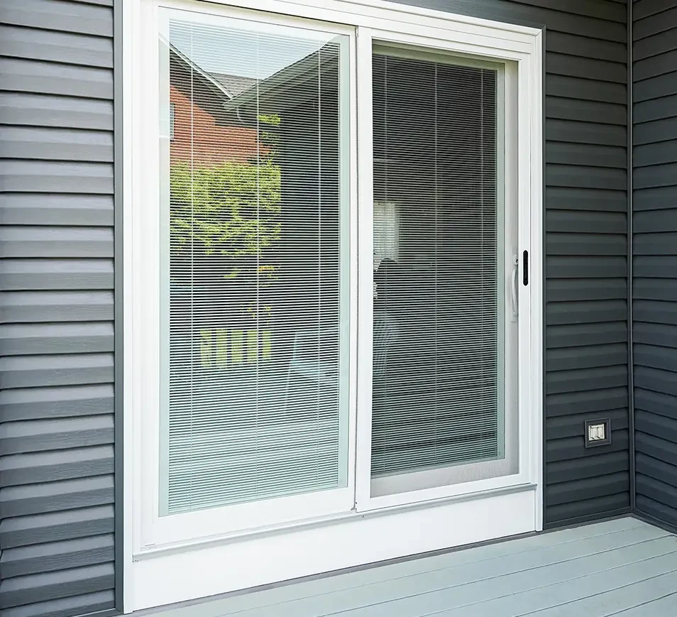 Close-up of a dark wooden front door with glass panels, surrounded by green plants and flowers.