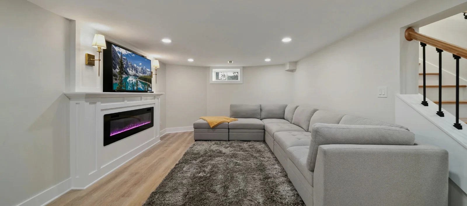 Modern basement with gray sectional sofa, TV over a fireplace, and a plush gray rug.