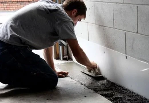 Handyman kneeling on the floor of a basement applying grout to the basement floor