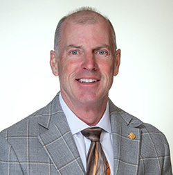 Person in a plaid suit and tie smiling against a plain background.