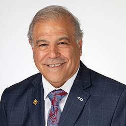 A person with gray hair wearing a suit and tie, against a plain background.