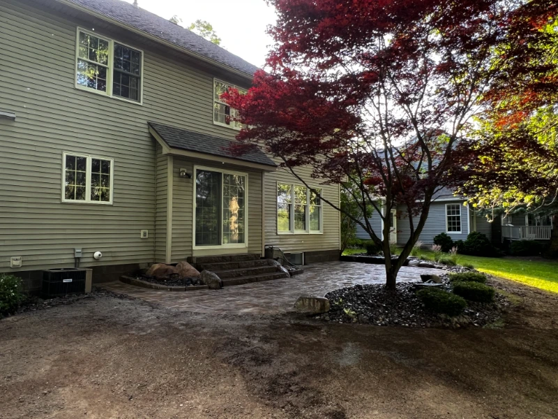 Stone patio with uplighting shining on large trees and lush greenery in the background at dusk.