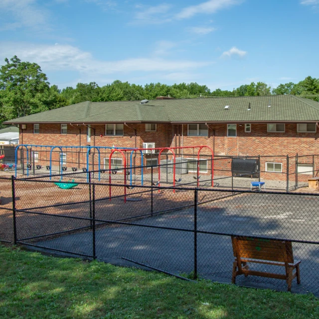 A fenced playground with swings in front of a brick building under a blue sky.
