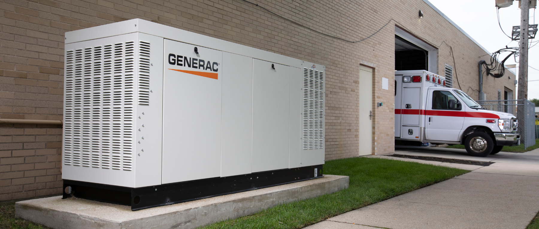Large Kohler generator outdoors beside a utility structure at dusk, under a transmission tower.