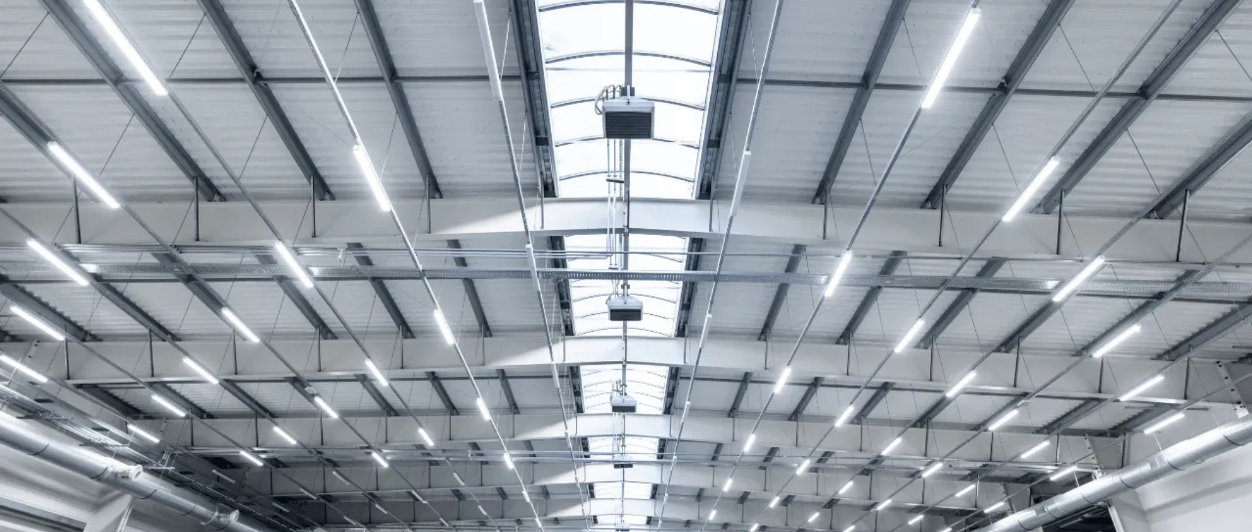 Modern industrial ceiling with metal beams, skylights, and bright overhead lighting.