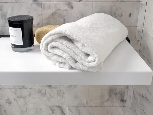 Minimalist bathroom with a white tub, beige tiles, towels, bottles, and framed wall art.