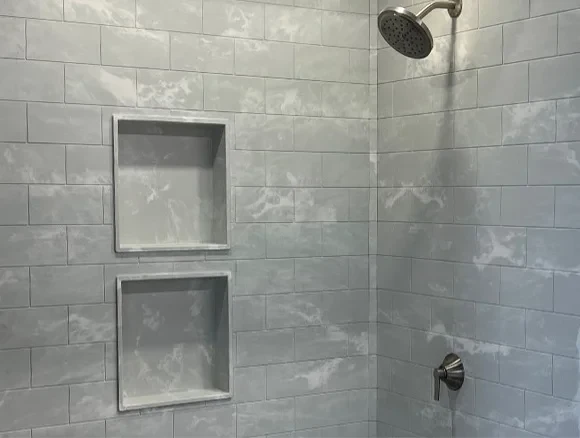 A white towel hangs on a silver towel rack, with a soap dispenser on a tiled bathroom wall.
