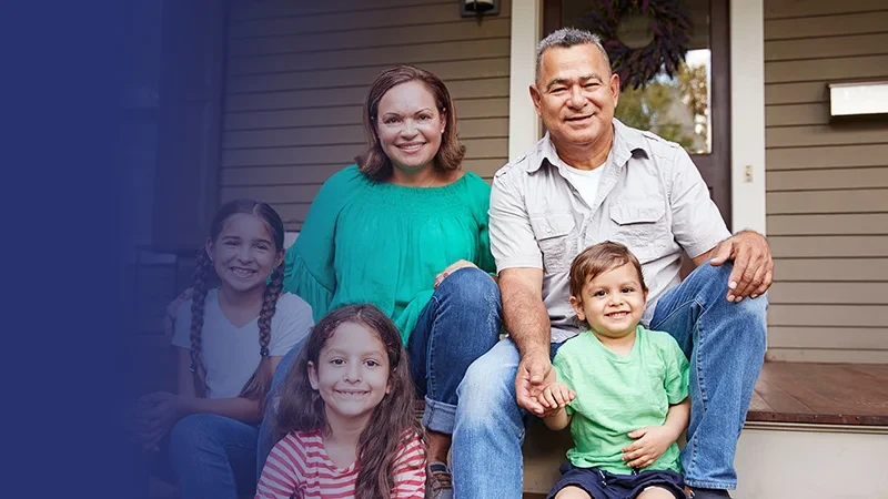 A family of five smiling and sitting together on the front porch of a house.