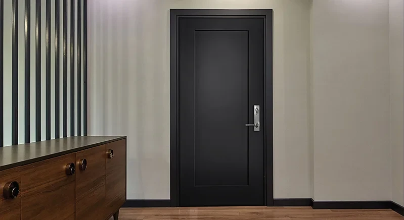 A black door with a silver handle in a modern room with striped walls and a wooden cabinet.