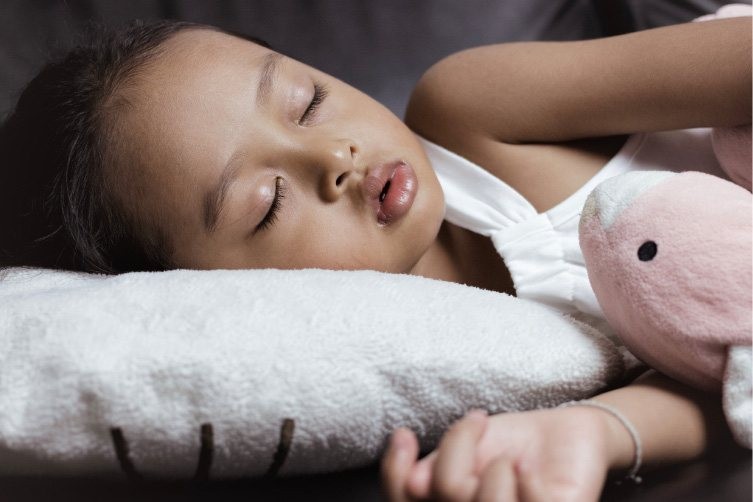 A young child peacefully sleeping on a white pillow, hugging a pink stuffed animal.