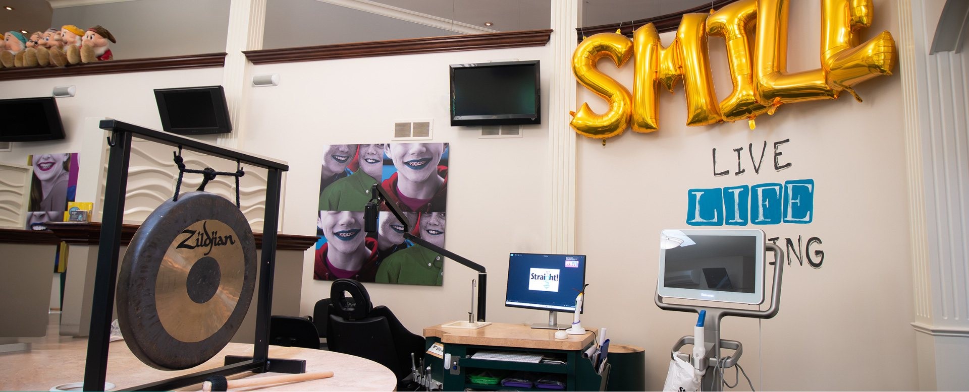 Dental office with SMILE balloons, posters of smiling kids, gong, and dental equipment.