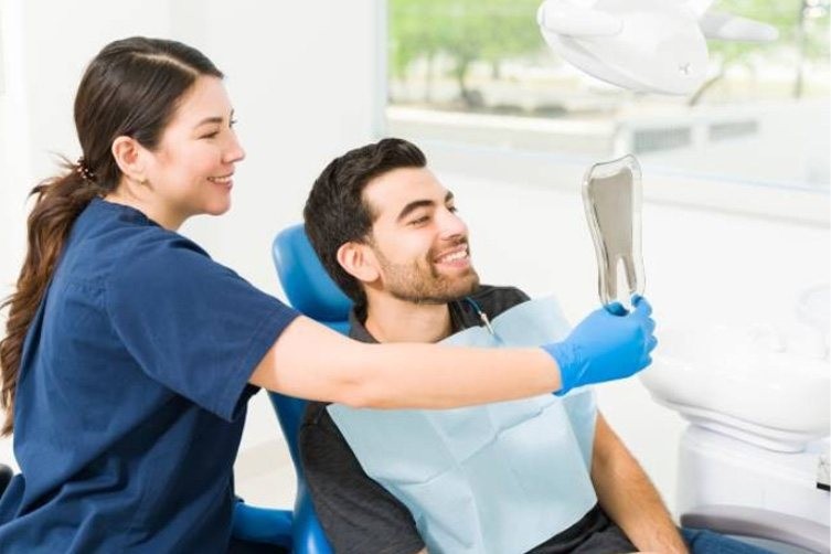 Dentist shows a smiling male patient his reflection in a mirror at a dental clinic.