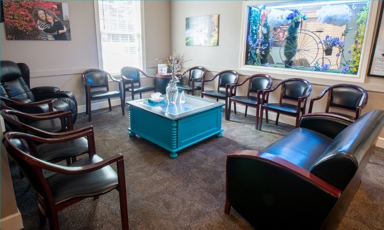 A waiting room with black chairs, a blue table, and a large window with decorative flowers.