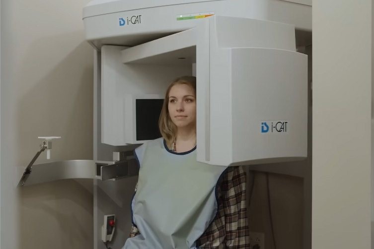 Woman wearing a lead apron undergoing a dental scan with an i-CAT 3D imaging machine.