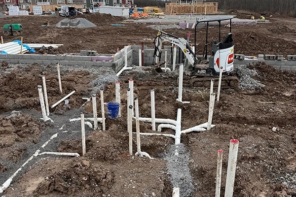 Plumbing pipes and a mini excavator at a muddy construction site for new buildings.