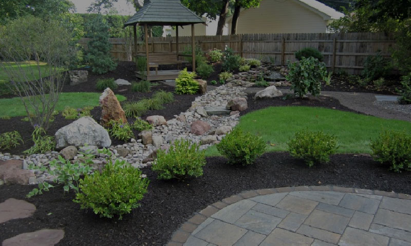 stone patio with mulch, grass, and small stones surrounding, gazebo in background