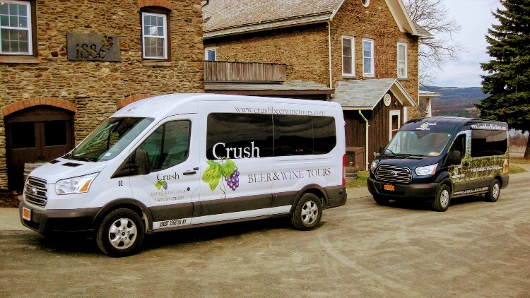 Two Crush Beer Wine Tours vans parked outside a stone building on a dirt driveway.