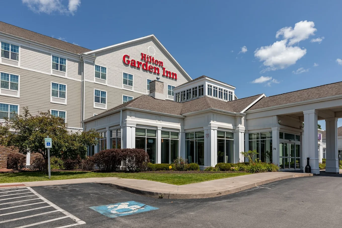 Exterior view of a Hilton Garden Inn hotel with clear skies and a visible handicap parking spot.