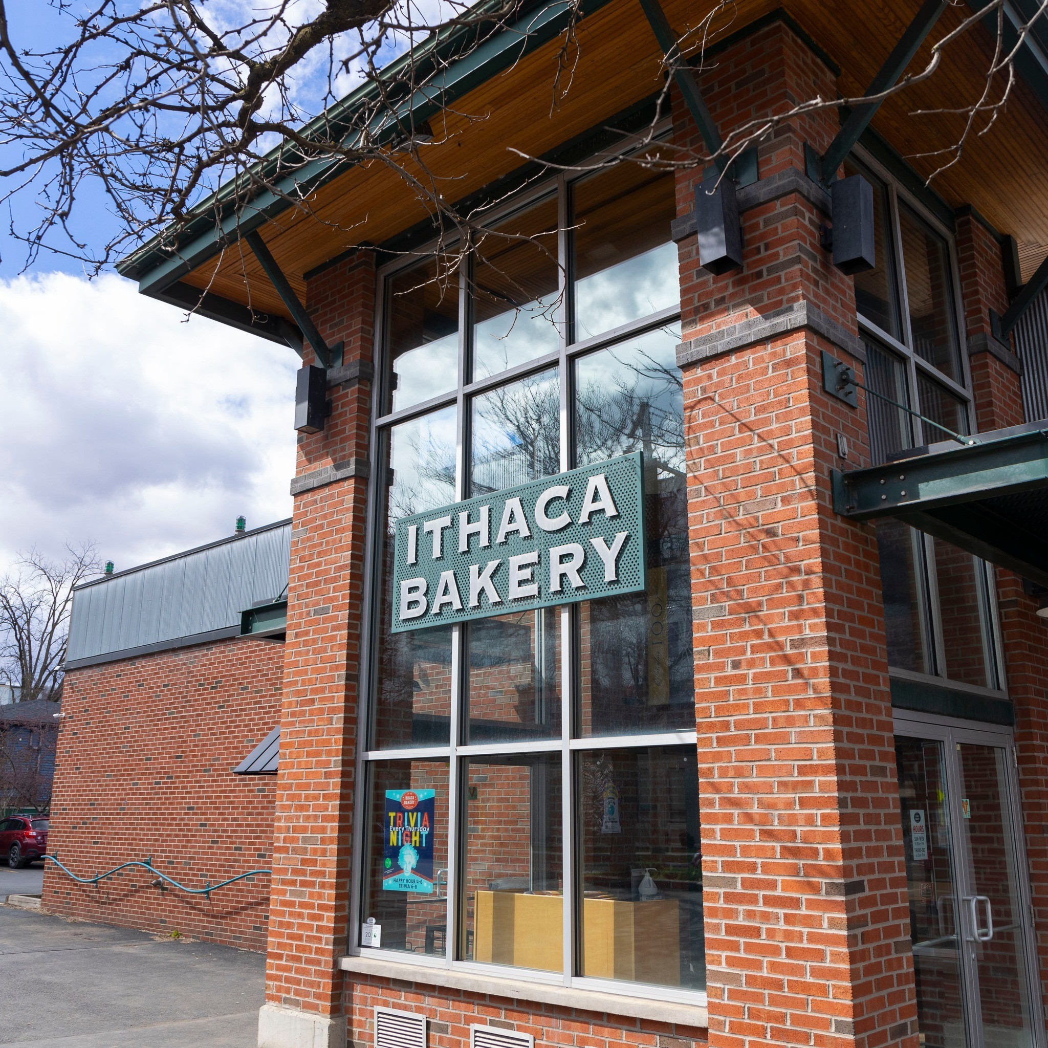 Exterior of Ithaca Bakery with large windows and a green sign on a brick building.
