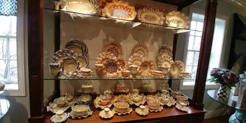 Colorful ceramic plates and bowls are displayed on glass shelves in front of two windows.