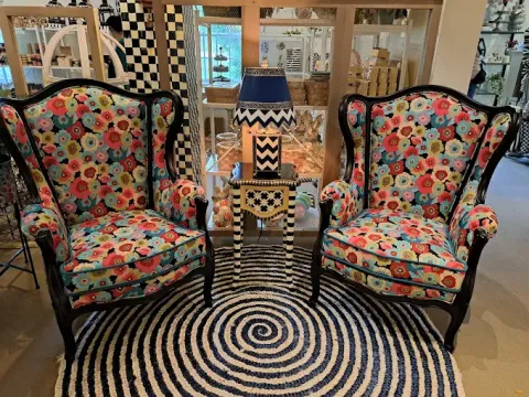 Two floral armchairs beside a lamp on a table, on a black and white spiral rug.