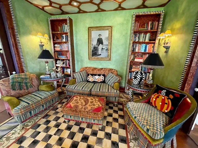 Colorful eclectic living room with striped furniture, checkered rug, and bookshelves on both sides.