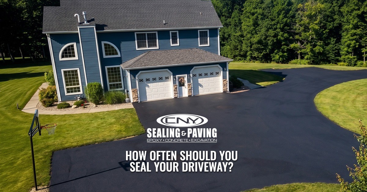 A freshly sealed black driveway in front of a blue house with text about driveway sealing.