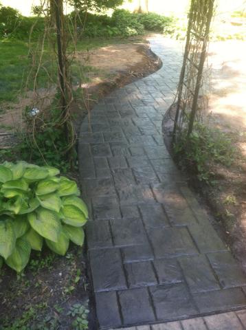 Curved stone garden path bordered by greenery and an archway, leading into sunlight.