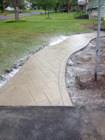 A newly constructed curved concrete walkway bordered by grass in a residential area.
