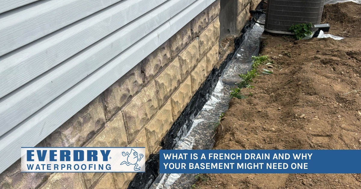 Close-up of a house foundation being waterproofed with a French drain beside exposed soil.