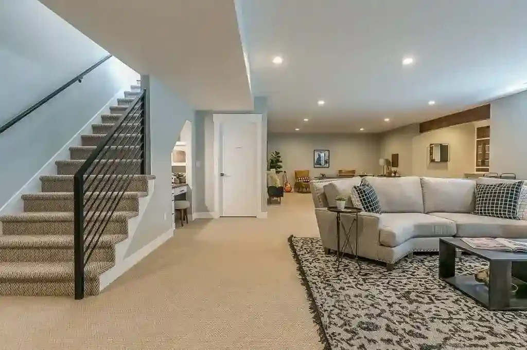 A modern basement with carpeted stairs, a sectional sofa, and a patterned area rug.