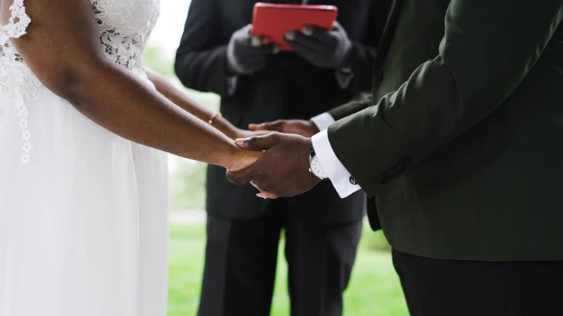 A bride and groom hold hands during a wedding ceremony, with an officiant standing behind them.
