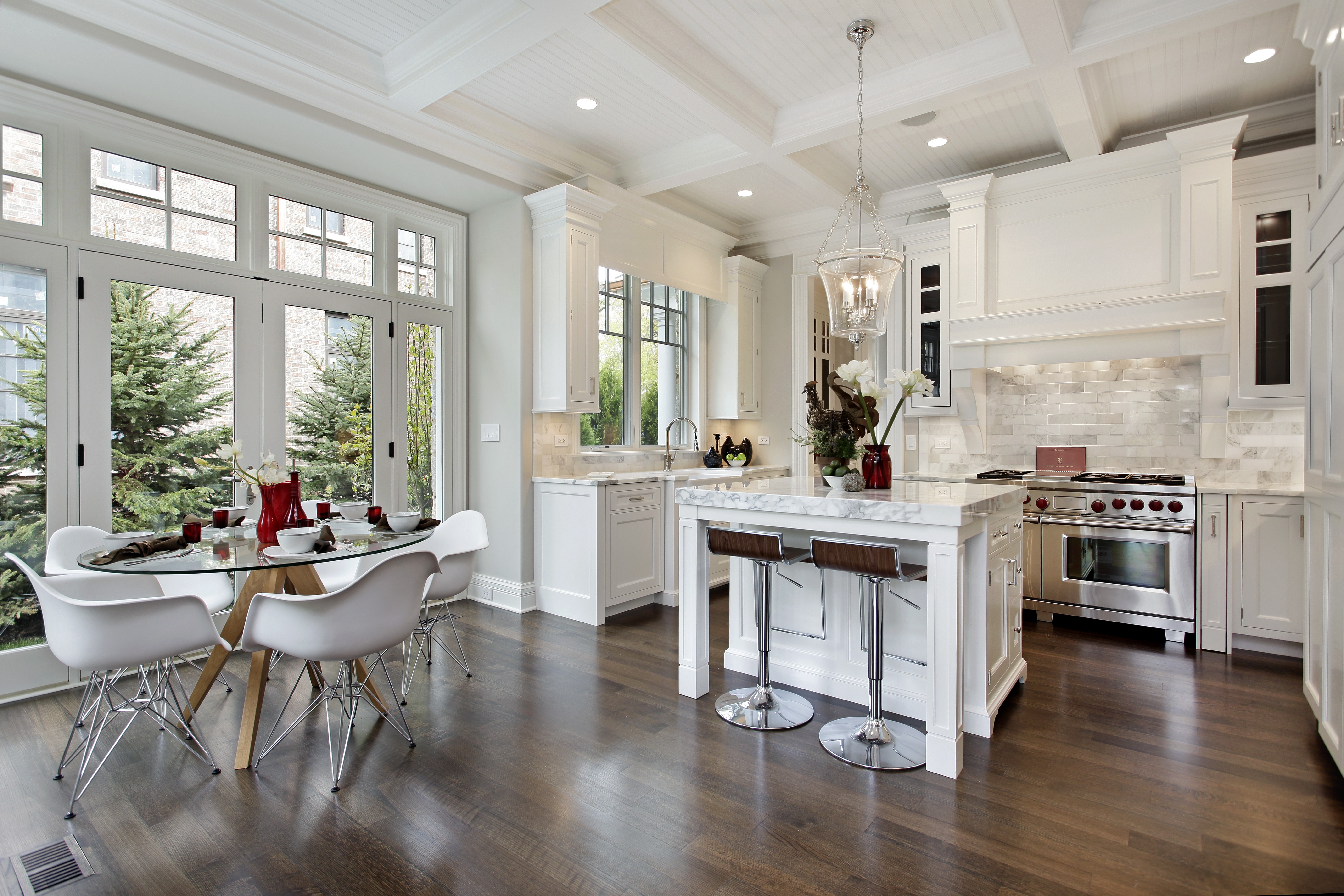 Bright modern kitchen with white cabinets, island seating, and dining area by large windows.